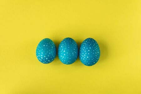 Blue speckled Easter eggs on bright yellow background, top view