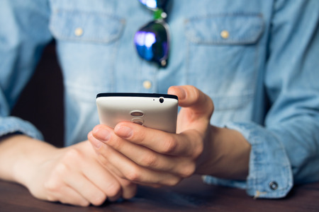 Woman using a mobile phone, she is dressed in a denim shirt and sunglassesの写真素材