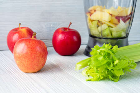 Apples, a bunch of celery, and a food processor on white table. Concept of healthy nutrition.の写真素材