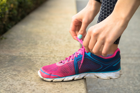 Female hands with manicure tie laces on pink and blue sneakers while jogging in the park