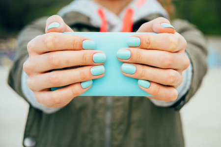 Female hands holding a mobile phone that is the same color as the manicure on her nailsの写真素材