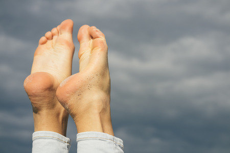 Barefoot female feet in the beach sand on a sky backgroundの写真素材