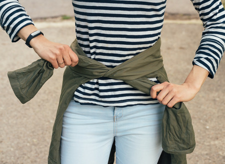 Woman in striped t-shirt tying the sleeves of the green jacket at the waist