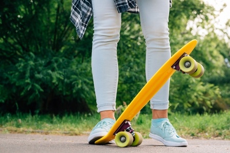 Girl in jeans and sneakers standing in a park next to yellow skateの写真素材
