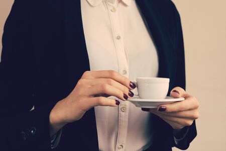 Woman in white blouse and black jacket holding a coffee cup in hand, a yellow toningの写真素材