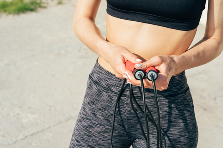 Close-up of a girl in a bra and sweat pants with a red skipping rope outdoors in sunlightの写真素材
