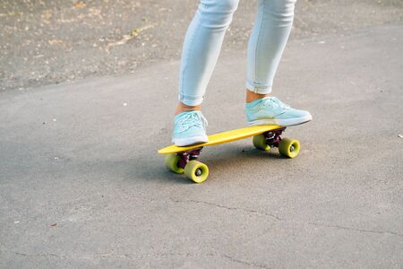 Close-up of female legs in jeans and sneakers riding a skateboard on the road