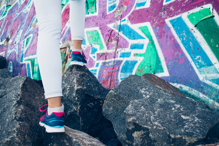 Female legs in sneakers and jeans climb over the rocks on the background of a graffiti wallの写真素材