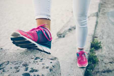 Female legs in sneakers and jeans standing on a concrete curb, toned imageの写真素材