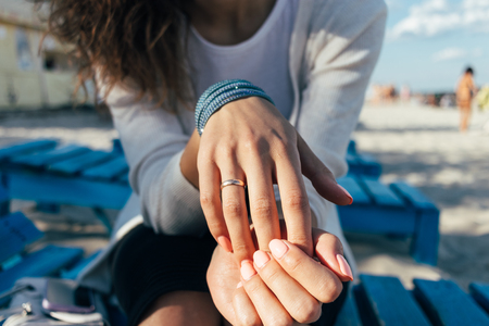 Close up of a Woman with a ring on her finger sitting on a bench on the beachの写真素材