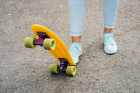 Female legs in jeans and sneakers standing near bright yellow skateboardの写真素材
