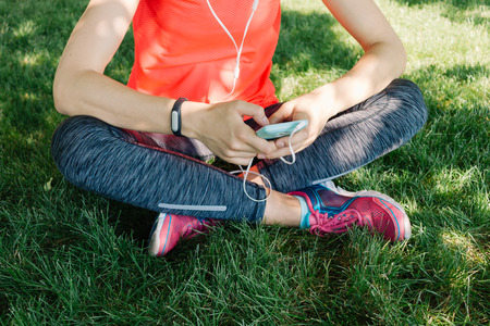 Girl in sports clothes listen to music on headphones sitting on the grass in the summer parkの写真素材