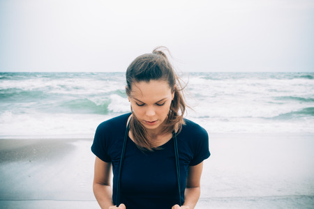 Attractive female athlete with a skipping rope on the beach in cold weather