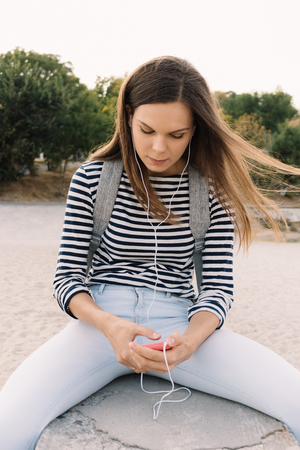 Beautiful girl in a striped T-shirt listening to music on the beach, vertical framingの写真素材