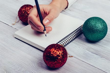 Woman sitting at a table with Christmas balls and writing in a notebook with a pencil, close-upの写真素材