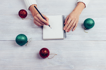 Woman writes in a notebook with a pencil, next on the table are Christmas tree balls, top viewの写真素材