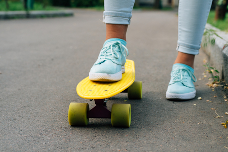 Close-up of female legs in blue jeans and sneakers standing on a yellow skateboard, low angle shootingの写真素材