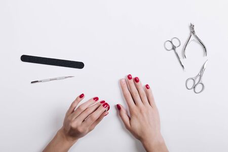 Women's hands with a red manicure scissors and nail file on a white table top viewの写真素材