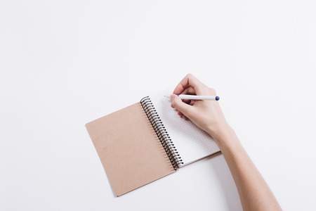 Female hand writes a pen in a notebook on a white table top viewの写真素材