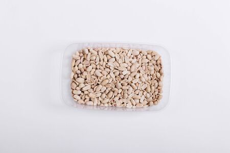 Plastic container with roasted peanuts on a white background, top view