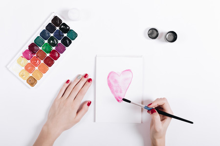 Top view of a woman's hands with red nail polish painted watercolor heart in notebook