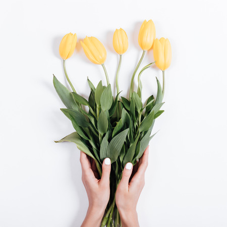 Top view of female hands with manicure holding a bouquet of yellow tulips on a white backgroundの写真素材