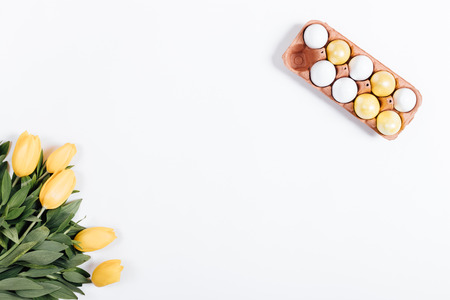 Top view of Easter eggs and yellow tulips on a white table, place for text