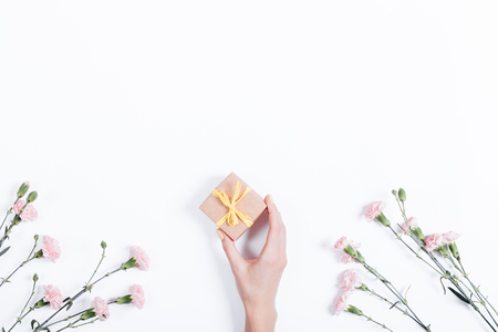 Little pink carnation on a white background and a woman's hand with a gift in a small box, space for text, top viewの写真素材
