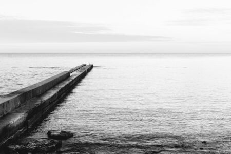 Black and white image of a concrete pier on the coast, minimalistic landscape