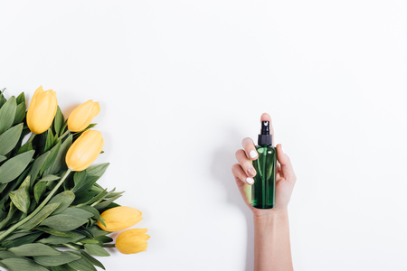 Female hand with manicure holds a green plastic bottle of water near yellow tulips, view from top, space for textの写真素材