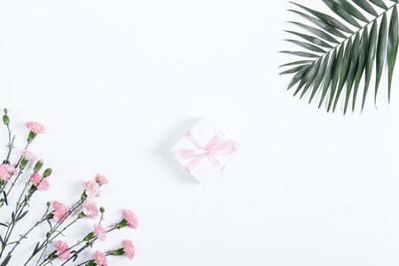 Small box with pink ribbon and flowers lie on a white table, top viewの写真素材