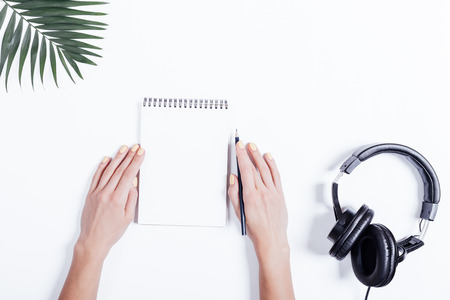 Top view of a female hands with a notebook and pencil, headphones and plant on white tableの写真素材