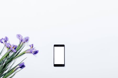 Bouquet of violet irises and mobile phone on a white table top view, copy spaceの写真素材
