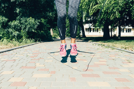 Close-up of female legs in sneakers jumping rope in summer outdoors, low angle shooting, soft focusの写真素材