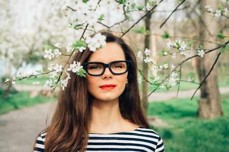 Portrait of beautiful young woman with glasses in the spring among flowers. Girl with long brown...