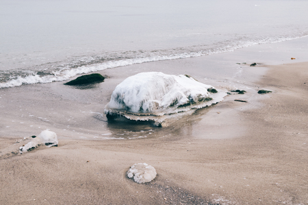 Icy stone is lying on the beach near the water in winterの写真素材