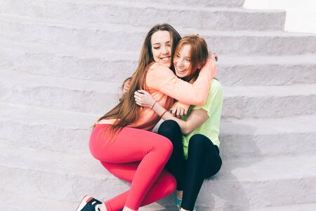 Two girlfriends in sportswear hugging and laughing at sunny day outdoors