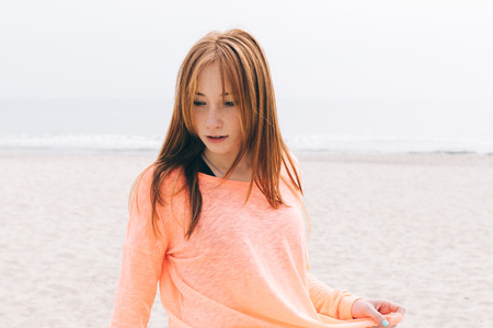 Portrait of a beautiful young red-haired girl on the beach in cloudy weatherの写真素材