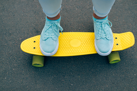Close-up of female legs in jeans and blue sneakers standing on a yellow plastic skateboard, top viewの写真素材