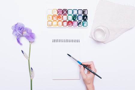 Female hand drawing in a notebook with watercolors, top viewの写真素材