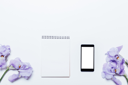 Blue flowers, mobile phone and notepad lie on a white background, top viewの写真素材
