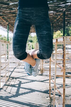 Vertical image of an athletic young woman doing pull-ups outdoors in the morning, close-up. Female...