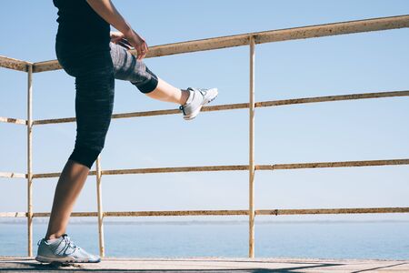 Young athletic woman doing stretching legs on the beach in the morning. Concept of a healthy lifestyle.の写真素材