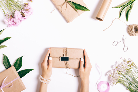 Female hands with a manicure hold a box with a gift and ribbon on a white table. Top view, preparation for the holiday.の写真素材