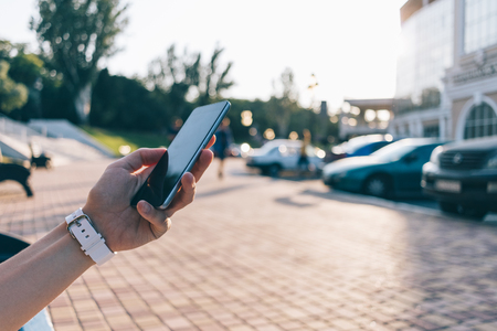 Mobile phone in woman's hand against city summer background, close-upの写真素材