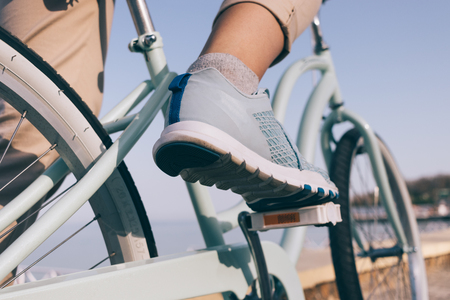 Female foot in a blue sneaker and a bicycle on the beach close-upの写真素材