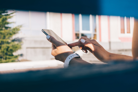 Close-up of a young woman sitting on a bench and enjoying a mobile phone in summerの写真素材
