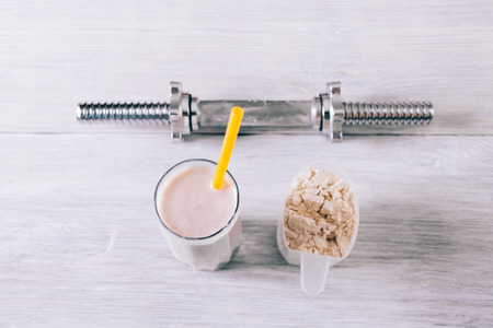 Protein cocktail in a glass, scoop and dumbbell on a white wooden table top viewの写真素材