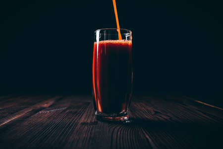 Tomato juice is poured into a full faceted glass on a black background, dark contrast lightの写真素材