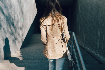 Woman in a beige jacket and jeans descends into the underpass, a view from the backの写真素材